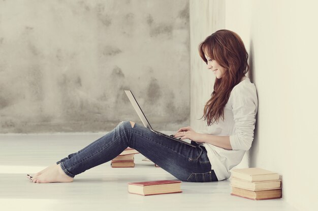 Schöne und charmante erwachsene Frau mit Laptop und Büchern