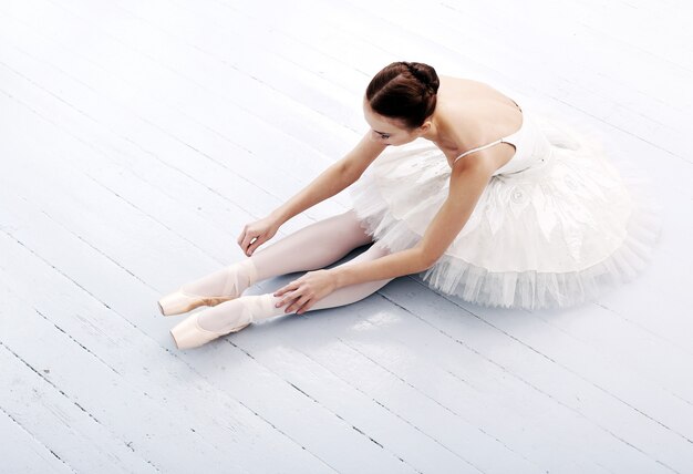 Schöne und wunderschöne Ballerina, die auf dem Boden sitzt