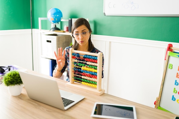 Schöne Vorschullehrerin, die Kindergartenkindern während eines Online-Unterrichts die Zahlen mit einem Abakus beibringt