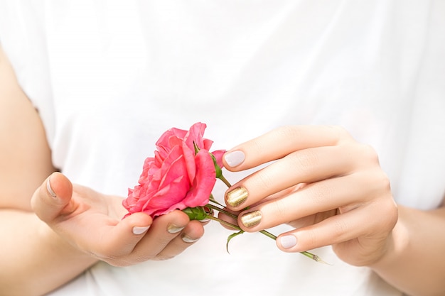 Schöne weibliche Hände mit perfektem goldenen und rosa Nageldesign halten frische Rosenblume