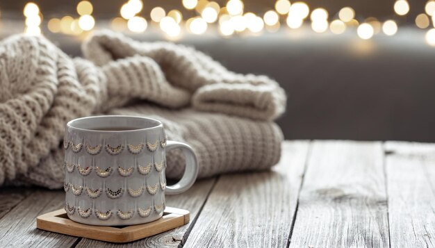 Schöne Weihnachtstasse und gestricktes Element auf unscharfem Hintergrund mit Bokeh