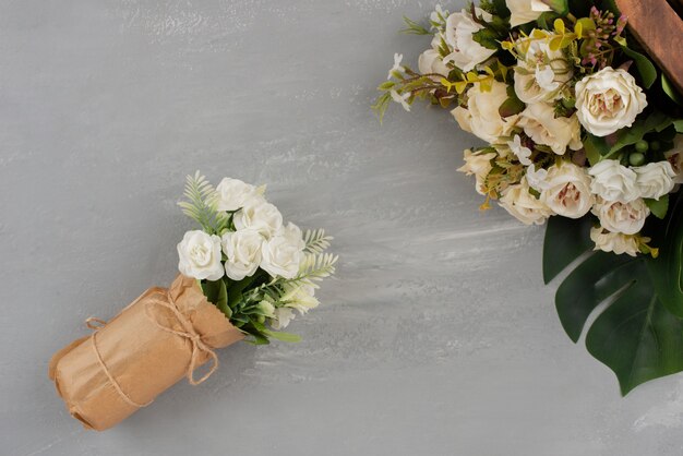 Schöne weiße Rosen auf Holzkiste und im Blumenstrauß auf grauer Oberfläche