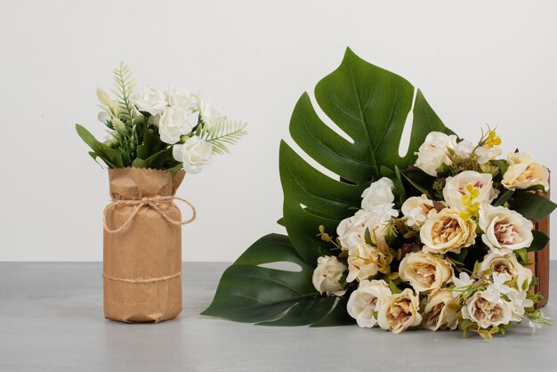 Schöne weiße Rosen auf Holzkiste und im Blumenstrauß auf grauer Oberfläche