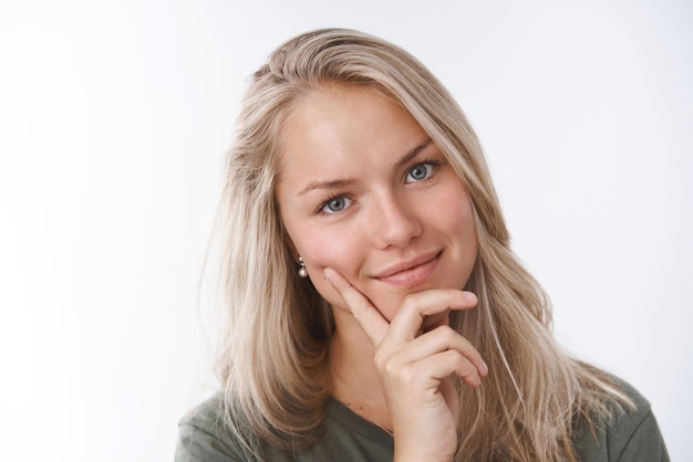 Schöne zarte und weibliche junge Frau, die den Kopf süß neigt und die Wange berührt, mit den Fingern, die romantisch in die Kamera lächeln