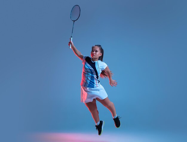 Schöne Zwergfrau, die im Badminton übt, einzeln auf Blau im Neonlicht
