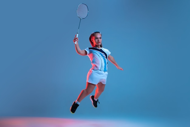 Schöne Zwergfrau, die im Badminton übt, isoliert auf Blau im Neonlicht