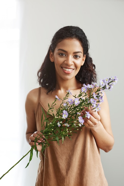 Schöner afrikanischer weiblicher Florist lächelnd, der Blumen hält. Weiße Wand.