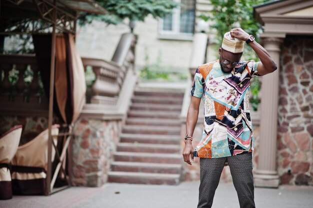 Schöner afroamerikanischer Mann mit traditioneller Kleiderkappe und Brille in der modernen Stadt