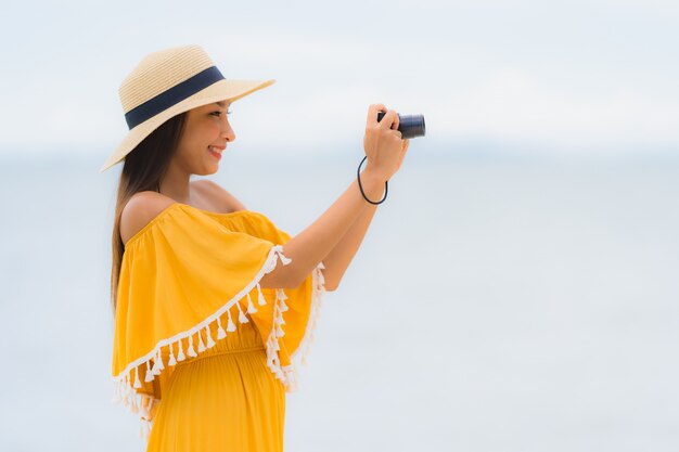 Schöner asiatischer Frauen-Abnutzungshut des Porträts mit glücklicher Freizeit des Lächelns machen herein ein Foto auf dem Strand und dem Meer in den Feiertagsferien