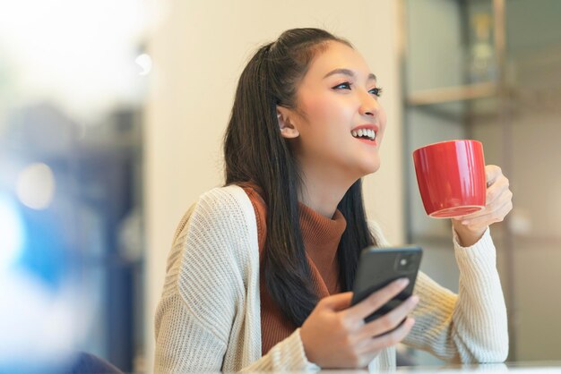 Schöner attraktiver asiatischer weiblicher Frischelächeln-fröhlicher Morgen, der mit Laptopkaffeearbeit von zu Hause aus mit Glück arbeitet, genießt Blick auf den Garten asiatische junge Frau mit Fensterlicht-Gartenhintergrund