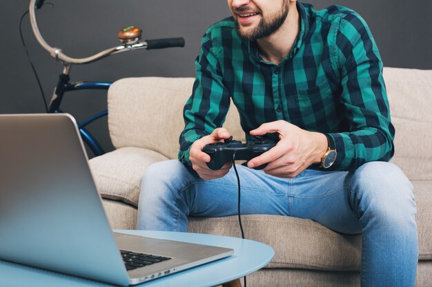 Schöner bärtiger Mann des jungen Hipsters, der zu Hause auf der Couch sitzt und Videospiel auf Notizbuch spielt