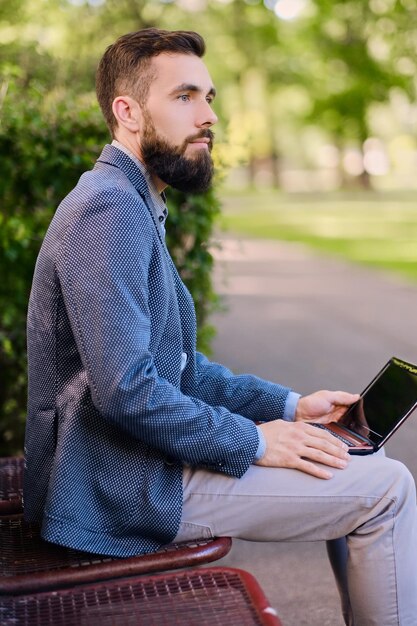 Schöner bärtiger Mann mit Laptop in einem Park.