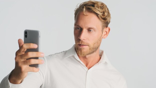 Schöner blonder bärtiger Geschäftsmann, der selbstbewusst über Video-Chat spricht, isoliert auf weißem Hintergrund