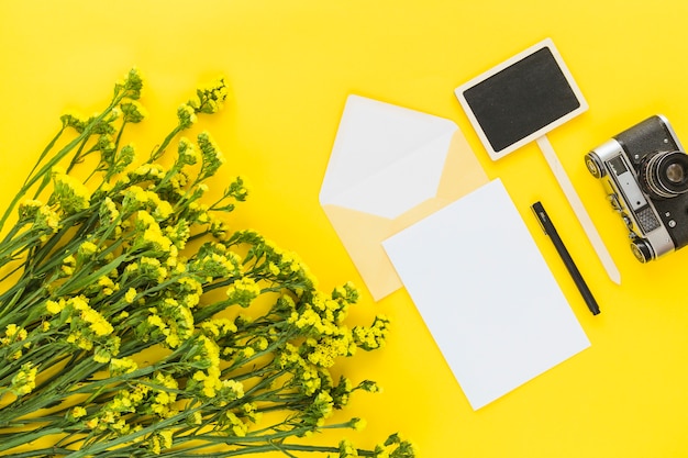 Schöner Blumenstrauß; Karte; Briefumschlag; Stift; Kamera und Plakat auf gelbem Hintergrund
