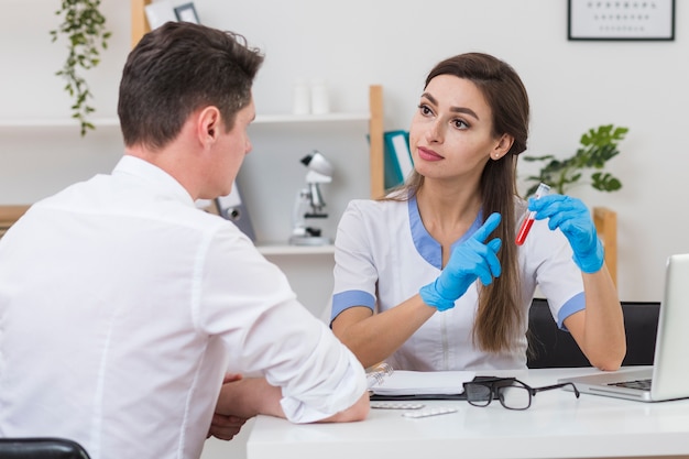 Schöner Doktor, der dem Patienten eine Blutprobe zeigt