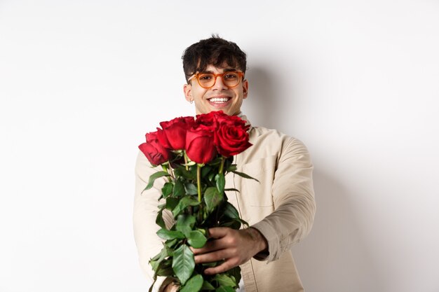 Schöner Freund, der Ihnen einen Rosenstrauß gibt, ein Überraschungsgeschenk für ein romantisches Date am Valentinstag machen und mit einem Liebhaber auf weißem Hintergrund stehen