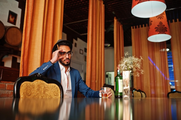 Schöner, gut gekleideter arabischer Mann mit Glas Whiskey und Zigarre posierte im Pub