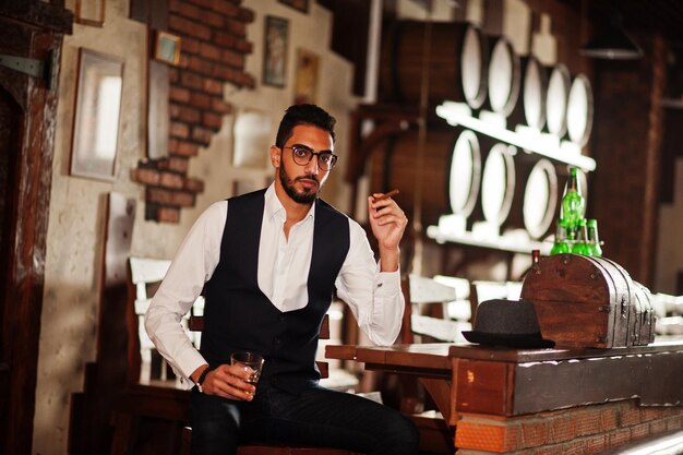 Schöner, gut gekleideter arabischer Mann mit Glas Whiskey und Zigarre posierte im Pub