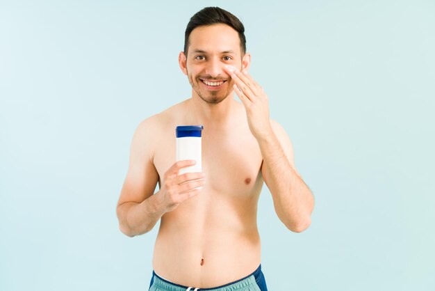 Schöner hispanischer Mann in seinen 20ern will keinen Sonnenbrand am Strand bekommen. Lateinischer Mann in einem Badeanzug, der Sonnencreme auf das Gesicht aufträgt