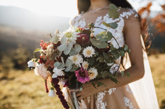 Schöner Hochzeitsstrauß aus Eukalyptus und bunten Blumen in den Händen des Mädchens im Freien am sonnigen Tag
