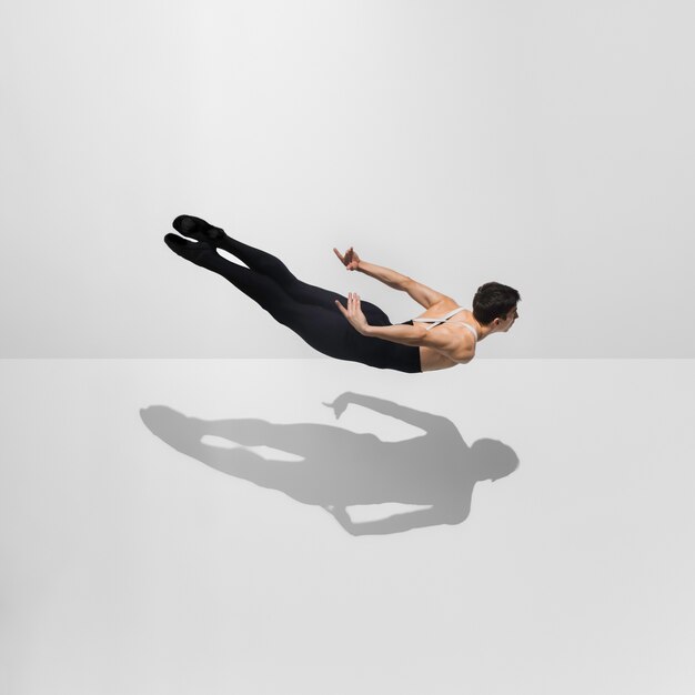 Schöner junger männlicher Athlet, der auf weißem Studio mit Schatten im Sprung, Luftfliegen übt