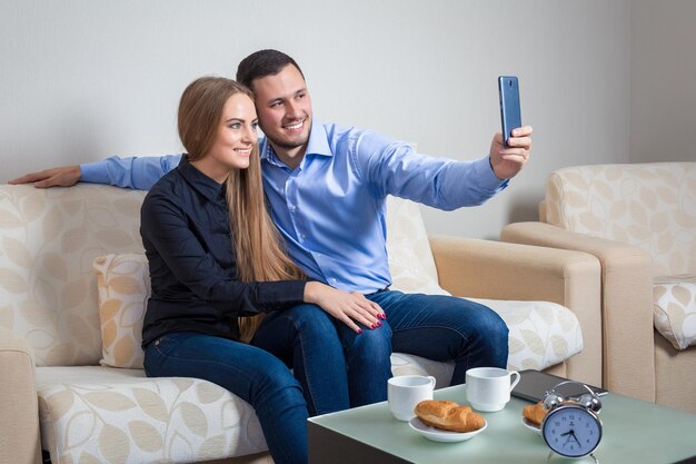 Schöner junger Mann und Frau, die Selfie mit Telefonkamera machen, glückliche Menschen, die ein Foto machen, das in die Kamera lächelt, bvsitting auf einem Sofa