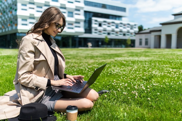 Schöner junger Student, der Laptop auf Gras im Campus verwendet