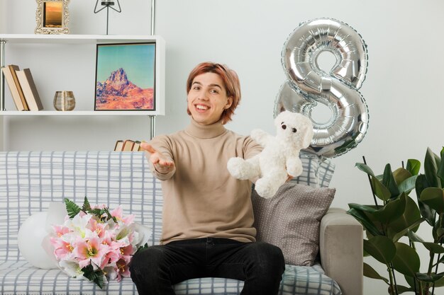 Schöner Kerl am glücklichen Frauentag mit Teddybär, der auf dem Sofa im Wohnzimmer sitzt