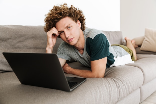 Schöner konzentrierter Mann liegt auf Sofa mit Laptop