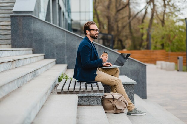 Schöner lächelnder bärtiger Mann mit Brille, der am Laptop arbeitet