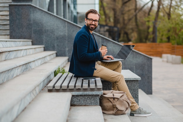 Schöner lächelnder bärtiger Mann mit Brille, der am Laptop arbeitet