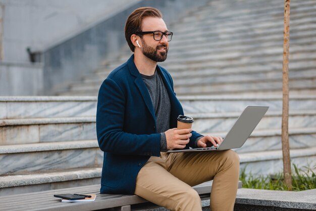 Schöner lächelnder bärtiger Mann mit Brille, der am Laptop arbeitet