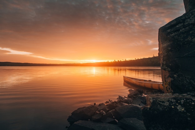Schöner langer Schuss eines Kanus auf einem See nahe Steinhügeln während des Sonnenuntergangs