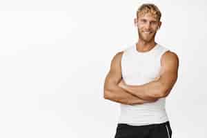 Kostenloses Foto schöner männlicher fitnesstrainer mit verschränkten armen und lächelndem, selbstbewusstem training im fitnessstudio, das über weißem hintergrund steht