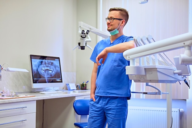 Schöner männlicher Zahnarzt in einem Raum mit medizinischer Ausrüstung im Hintergrund.