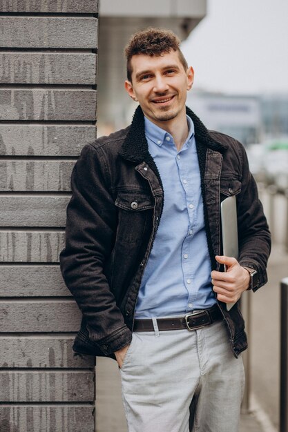 Schöner Mann, der auf der Straße steht und Laptop hält