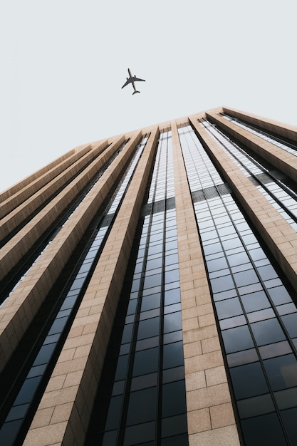 Schöner niedriger Winkelschuss eines hohen Geschäftsgebäudes mit einem Flugzeug, das über Kopf fliegt