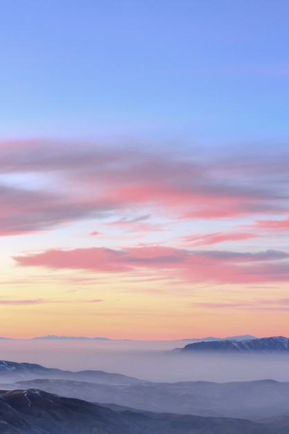 Schöner pastellfarbener Sonnenuntergang über den felsigen Bergen, die in der Wolke bedeckt werden