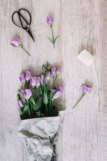 Schöner purpurroter Eustoma blüht Blumenstrauß mit Scissor und weißer Spule auf hölzernem Hintergrund