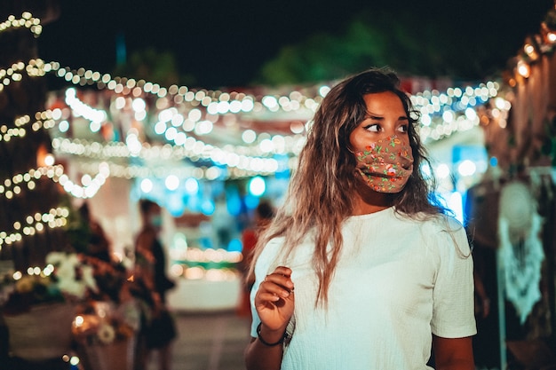 Schöner Schuss der gebräunten europäischen Frau, die eine Blumenmaske an einem Vergnügungspark trägt