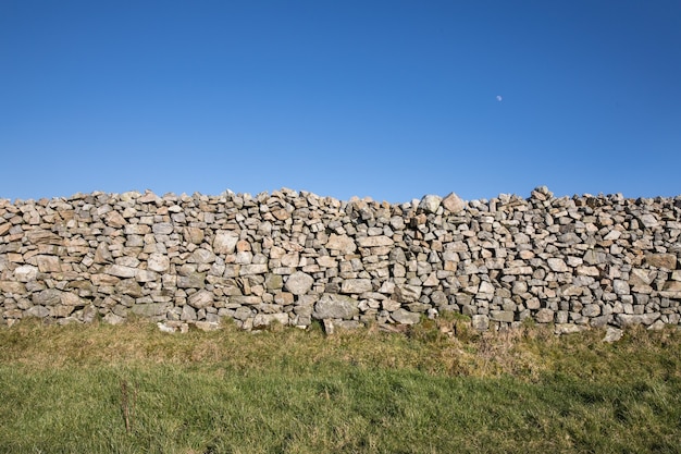 Schöner Schuss der Steinmauer in einem grünen Feld unter einem klaren Himmel