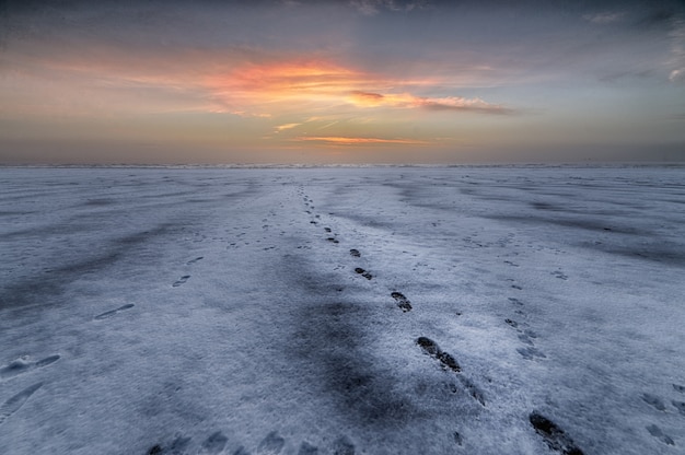 Schöner Schuss des Sonnenuntergangs über dem Strand mit Fußspuren, die zum Meer führen