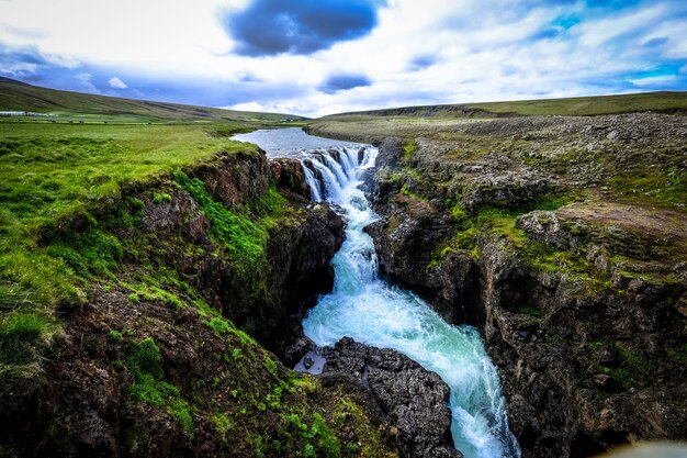 Schöner Schuss des Wasserfalls, der in der Mitte der felsigen Hügel unter einem bewölkten Himmel fließt