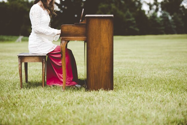 Schöner Schuss einer Frau, die das Klavier in einem Grasfeld mit einem unscharfen Hintergrund spielt