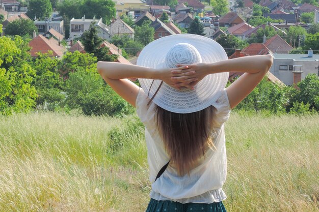 Schöner Schuss einer Frau, die einen weißen Hut ohrt und die Aussicht und die frische Luft in einem Grasfeld genießt