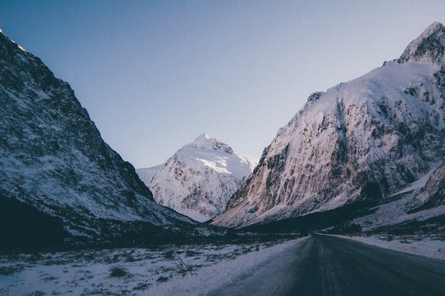 Schöner Schuss einer leeren Straße, die durch hohe felsige Berge geht, die mit Schnee bedeckt sind