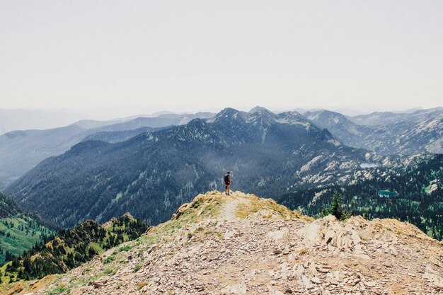 Schöner Schuss einer Person, die am Rand der Klippe mit bewaldeten Bergen steht