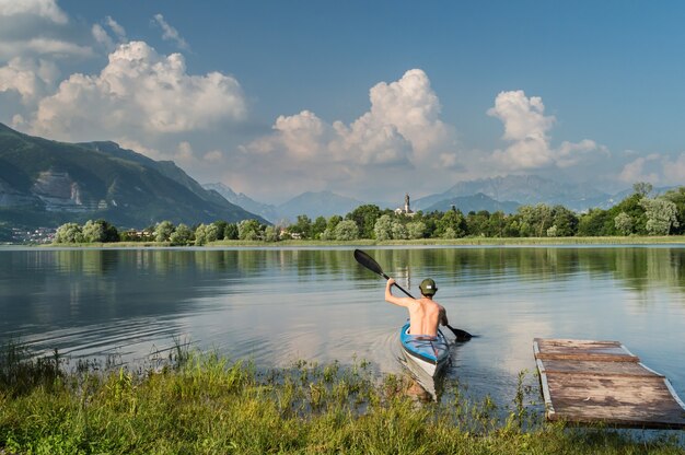 Schöner Schuss einer Person, die ein Boot auf dem See rudert, umgeben von Bäumen und Bergen