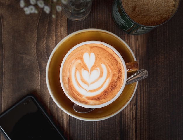 Schöner Schuss einer Tasse Cappuccino mit einem weißen Herzmuster auf einem Holztisch