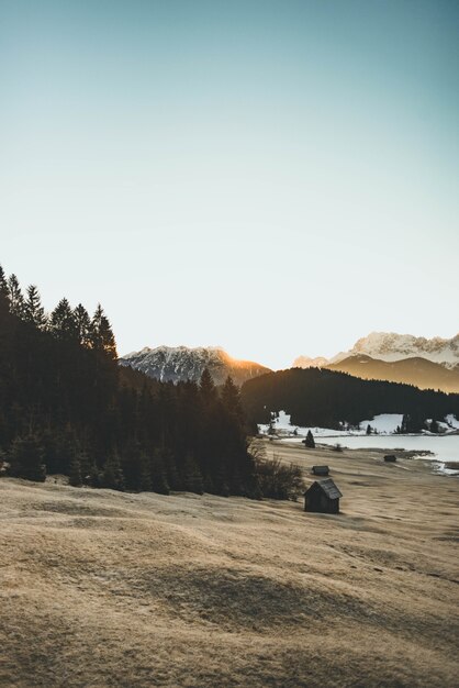 Schöner Schuss eines Hügels mit Bäumen und einer hölzernen Hütte und Bergen im Hintergrund